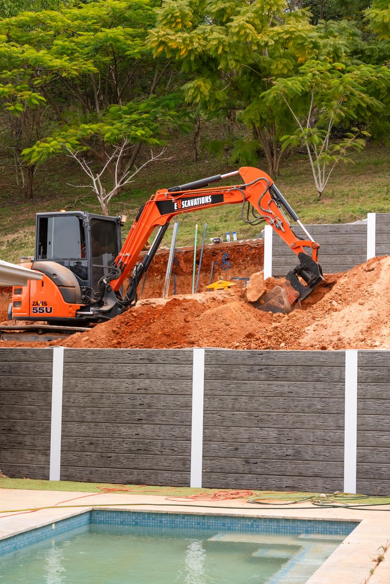 Excavator digging behind retaining wall