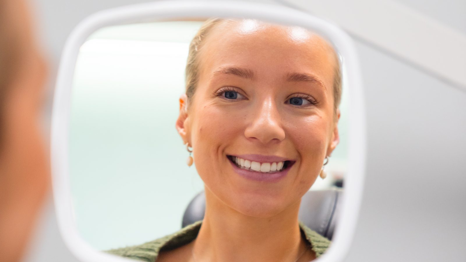Dental patient seeing her smile in a hand mirror at the practice
